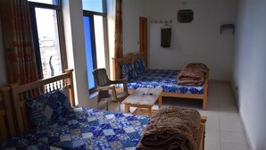 A room with two beds, a wooden chair, a small table, and a window with curtains. - Marwa Hotel and Restaurant (Abbottabad)