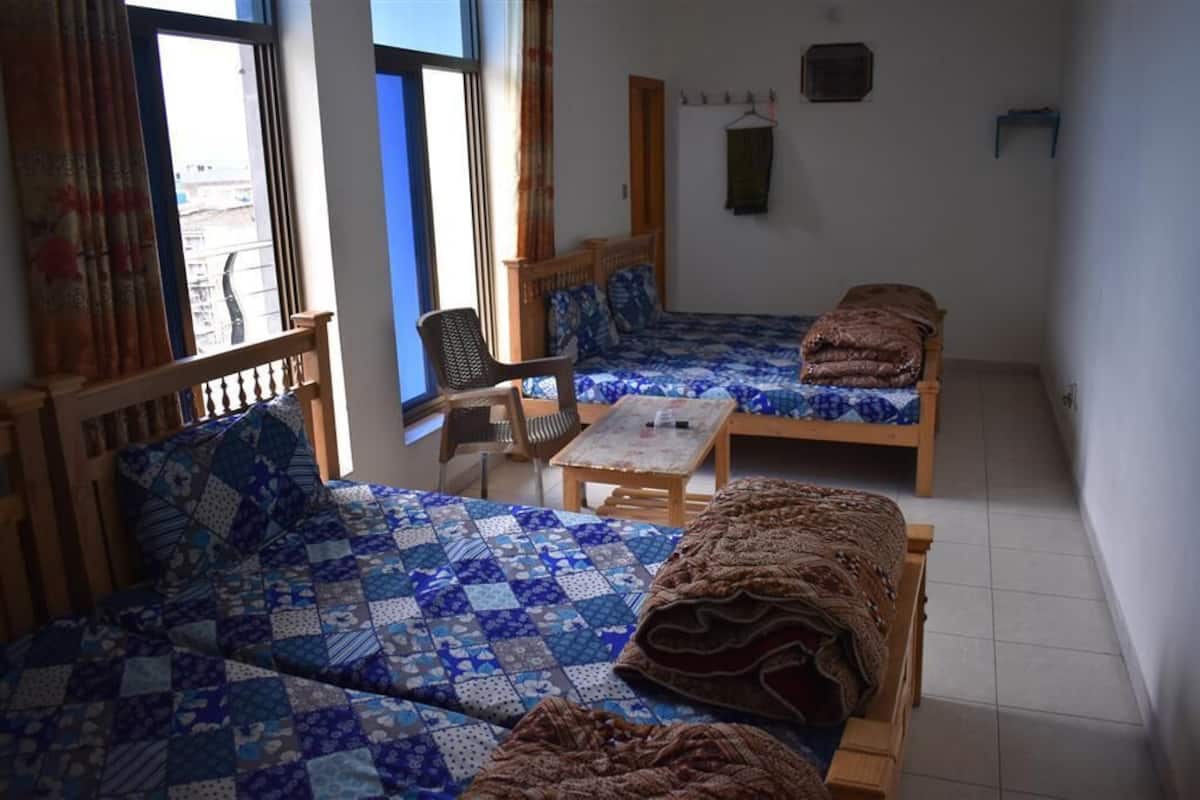 A room with two beds, a wooden chair, a small table, and a window with curtains.
