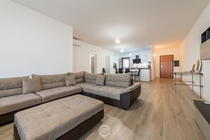 Uma sala de estar moderna com um sofá seccional, um banquinho pequeno e uma cozinha ao fundo.