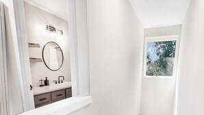 A modern staircase with a built-in light fixture, leading to a bathroom with a vanity, mirror, and a window.