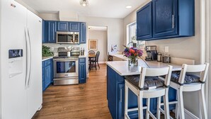 A modern kitchen with blue cabinets, stainless steel appliances, and a central island with bar stools.