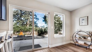 A room with a sliding glass door leading to a backyard, a wooden floor, a small table with a shelf, and a wall-mounted picture.