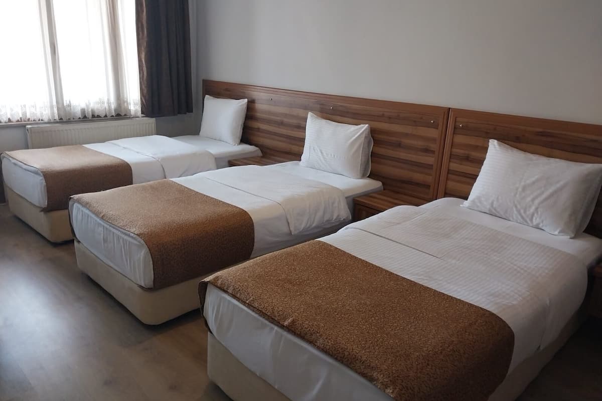 A hotel room with three beds, each with a wooden headboard and white bedding.