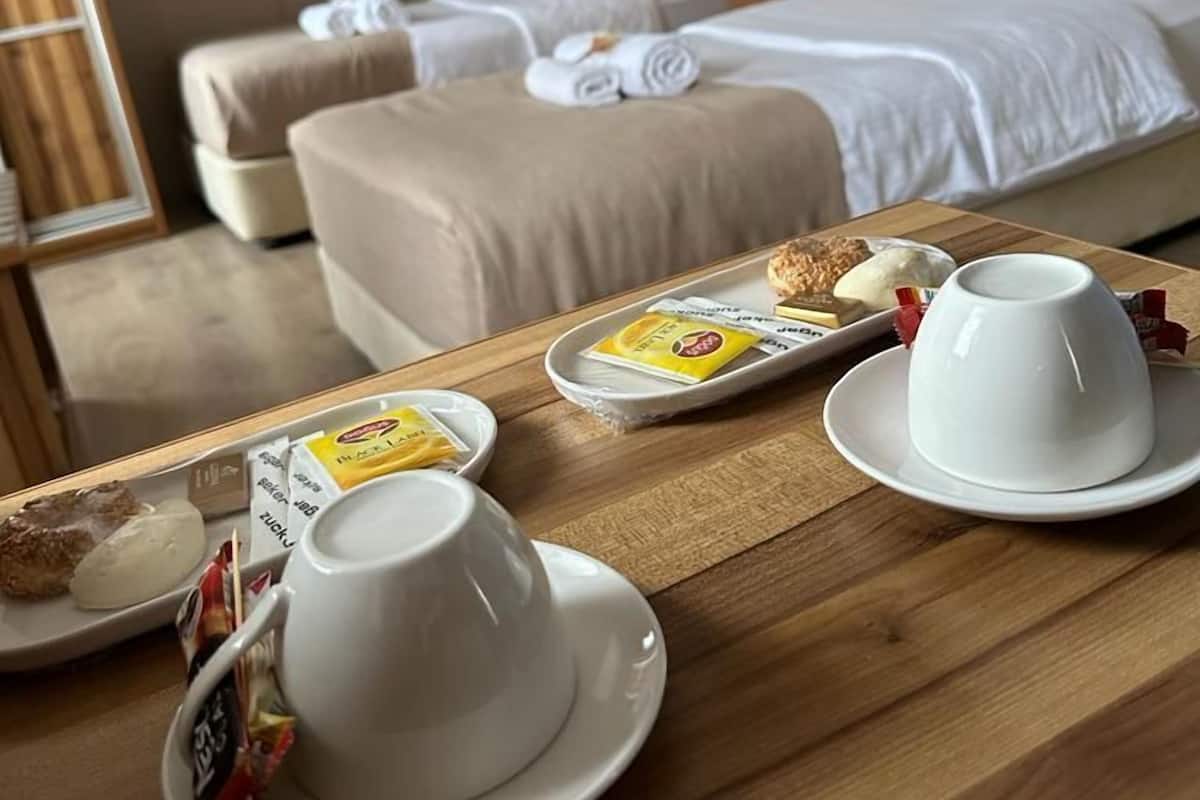 A hotel room with two beds, a wooden table with breakfast items, and a framed picture on the wall.