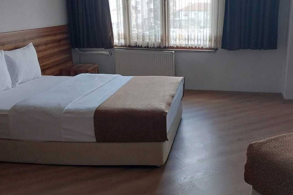 A hotel room with a bed, a bedside table, a window with curtains, a radiator, and a television.