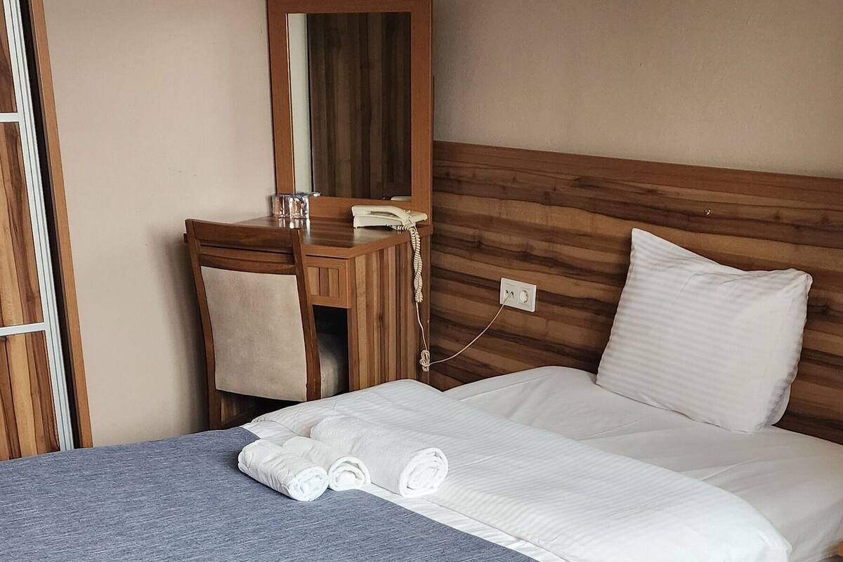 A neatly made bed with a blue blanket and white linens, a wooden headboard, a wooden desk with a telephone, and a mirror.