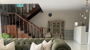 A green sofa with white cushions in a room with a staircase, a cabinet, and a radiator. - Park Otel (Düzce)