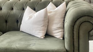 A green upholstered sofa with white cushions in a room with a wooden staircase and a white brick wall. - Park Otel (Düzce)