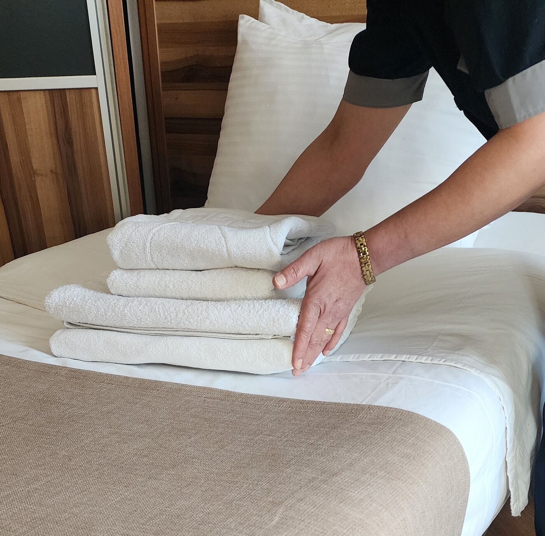 A neatly made bed with a stack of folded towels and a hand adjusting the pillows.