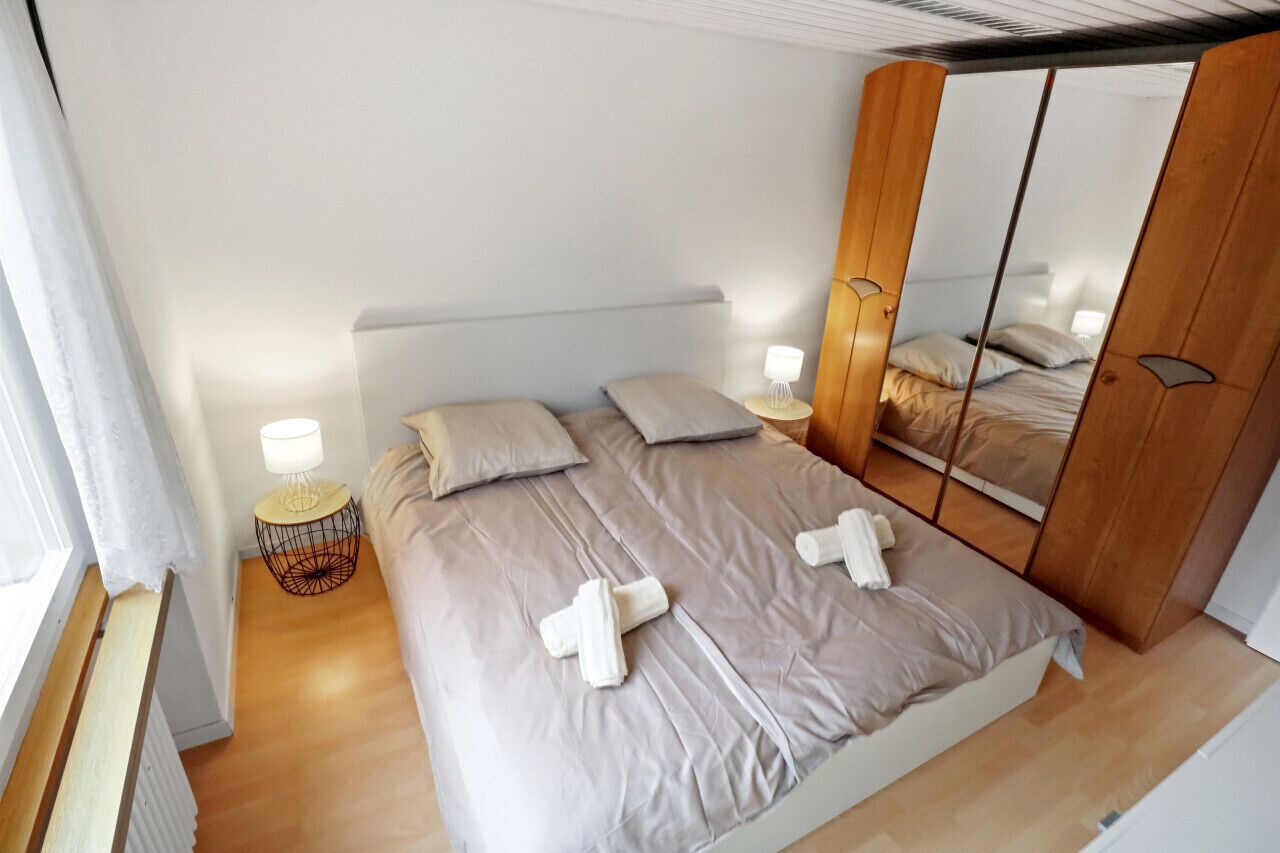 A bedroom with a bed, bedside lamps, a mirror, and a wardrobe.