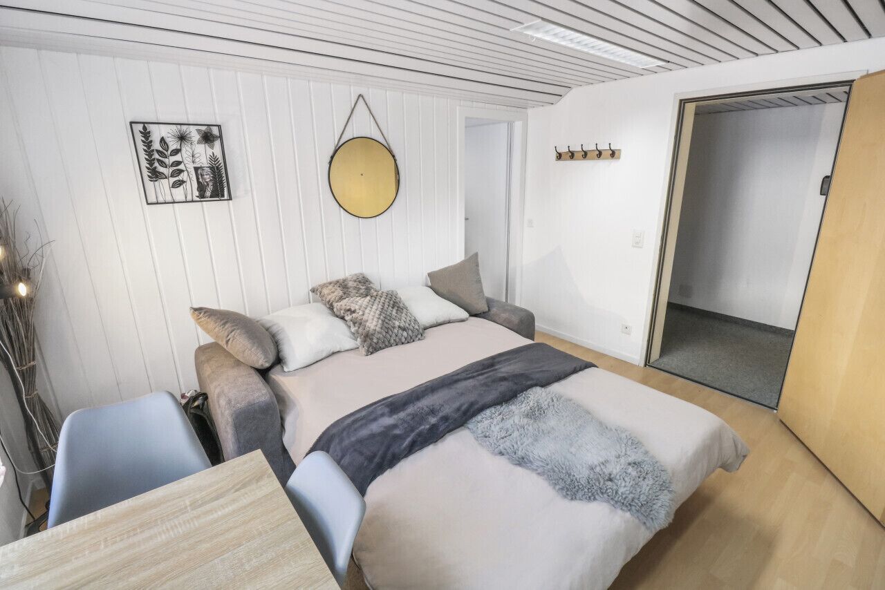 Un dormitorio moderno con una cama, mesitas de noche, un espejo circular colgante y una obra de arte en la pared.