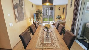 A dining area with a long table, chairs, a vase of flowers, and a hanging light fixture. - Nice apartment near the center (Martigny)
