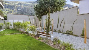 A modern outdoor area with a well-maintained lawn, a gravel path, and a wooden bench. - Nice apartment near the center (Martigny)