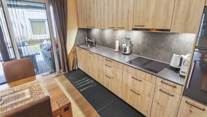 A modern kitchen with wooden cabinets, a black countertop, and a refrigerator. - Nice apartment near the center (Martigny)