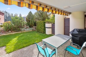 A patio with a table and chairs, a grill, and a covered area with a striped awning. - Superb apartment with free covered parking (Lens)