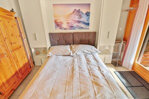 A bedroom with a bed, a wooden wardrobe, a painting of a mountain landscape, and a window with curtains. - Excellent apartment with free covered parking (Lens)