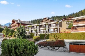 A row of chalet-style buildings with balconies, surrounded by well-maintained gardens and a mountain backdrop. - Superb apartment with free covered parking (Lens)