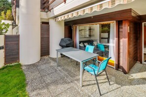 An outdoor patio with a table and chairs, a grill, and a sliding glass door leading to a covered area. - Superb apartment with free covered parking (Lens)