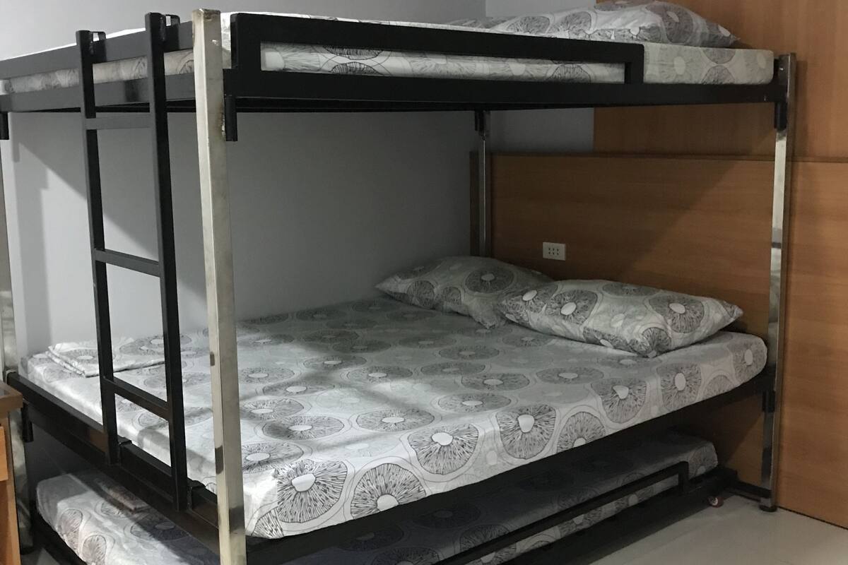 Ein Etagenbett mit gemustertem Bettzeug und Kissen, eine Holztür und ein gefliester Boden.