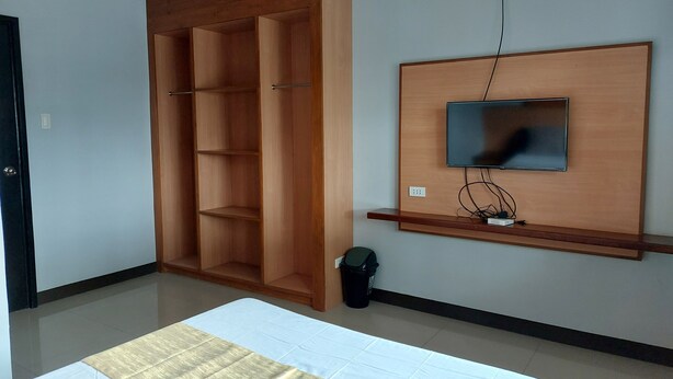 Une chambre à coucher avec un lit, une armoire en bois, un téléviseur fixé au mur et une poubelle.