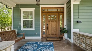 Un portico con una panca di legno, un tappeto decorato e una porta verde.
