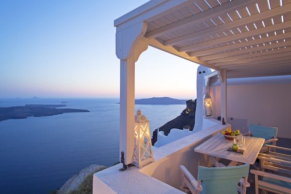 A terrace with a table, chairs, and a lantern overlooking a body of water.