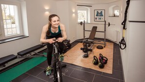 Ett gym med träningsredskap, en bänk, ett ställ för vikter och en yogamatta.