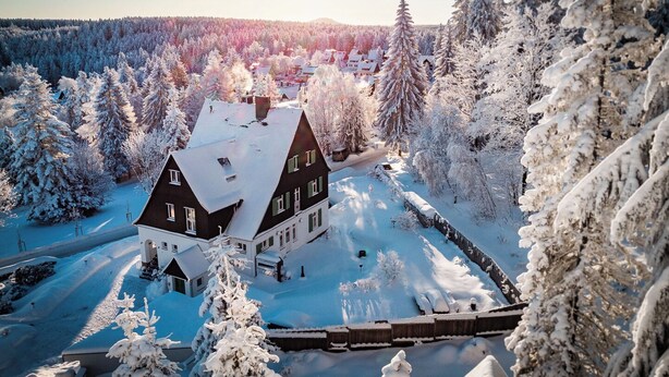 En stor byggnad med ett mörkt tak, omgiven av snötäckta träd och en klar himmel.
