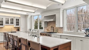 A spacious kitchen with a large island, white cabinetry, and a view of trees through large windows. - Private Mountain Estate | 7 Min to Okemo (Ludlow)