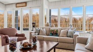 A cozy living room with a large window, a sofa, a coffee table, and a sign on the wall. - Private Mountain Estate | 7 Min to Okemo (Ludlow)