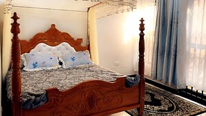 A four-poster bed with a wooden headboard, a patterned bedspread, and decorative pillows. - Cosy Family Home (Kampala)