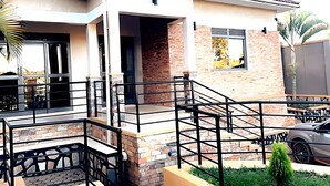 A modern two-story house with a brick facade, a balcony with a metal railing, and a car parked in the driveway. - Cosy Family Home (Kampala)