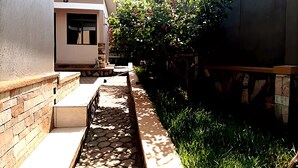 A narrow pathway leading to a house with a stone wall on one side and a brick wall on the other. - Cosy Family Home (Kampala)