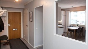 Un pasillo estrecho con una puerta de madera, un cuadro enmarcado y una pequeña zona de estar con una silla y una mesa.