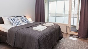 Habitación de hotel con cama, almohadas, una ventana con cortinas y vistas al exterior.