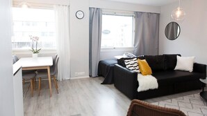 Una sala moderna con comedor, un sofá negro con cojín blanco y amarillo, un espejo redondo y un reloj en la pared.