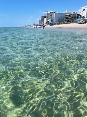 Une plage avec une eau claire, des bâtiments et des parasols.