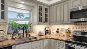 A kitchen with white cabinets, a stainless steel stove, and a window with a view of palm trees.