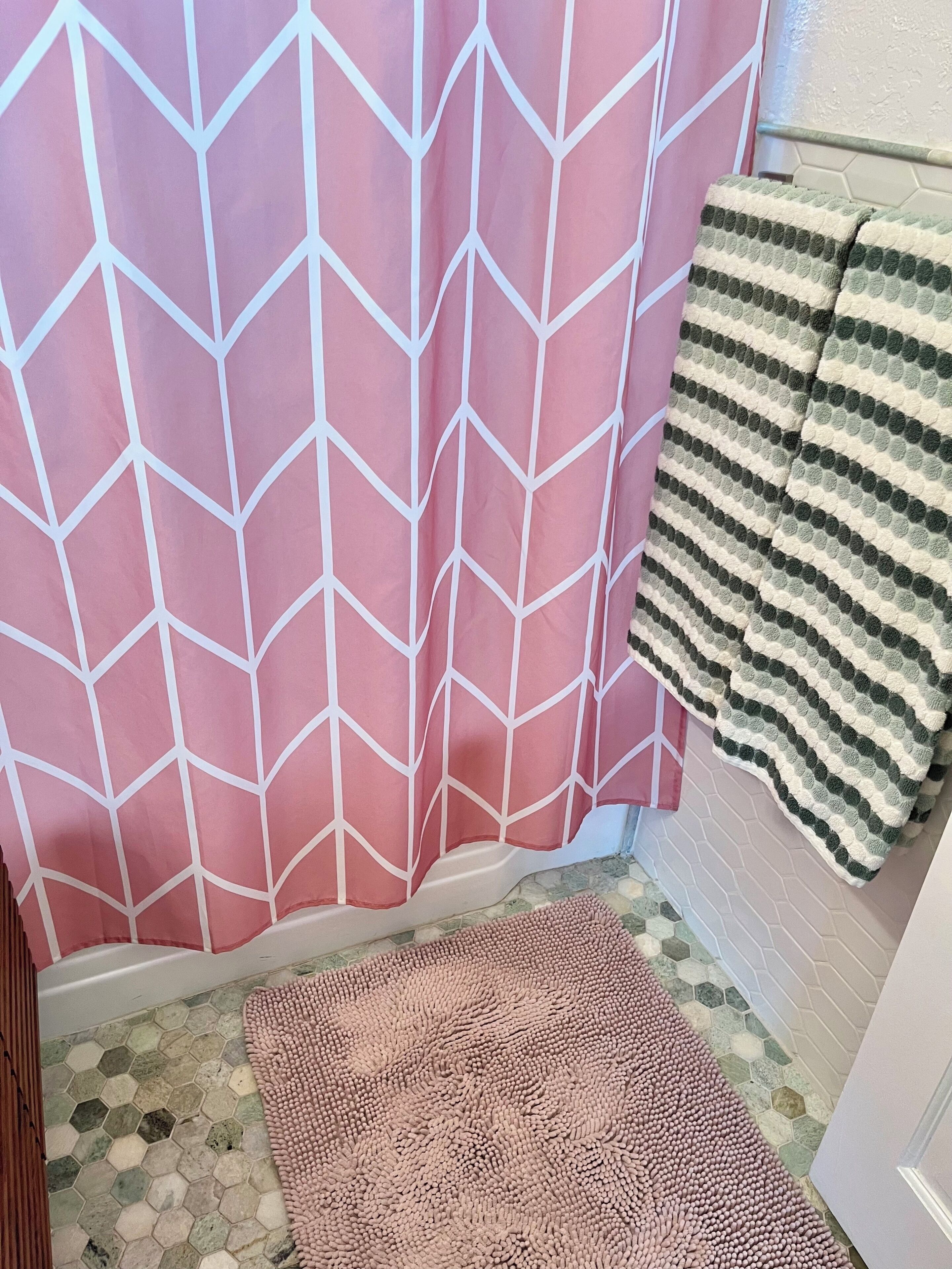 Un bagno con tenda da doccia a motivi a zig-zag rosa, un asciugamano a righe, un tappeto rosa con texture e pavimento in piastrelle esagonali.