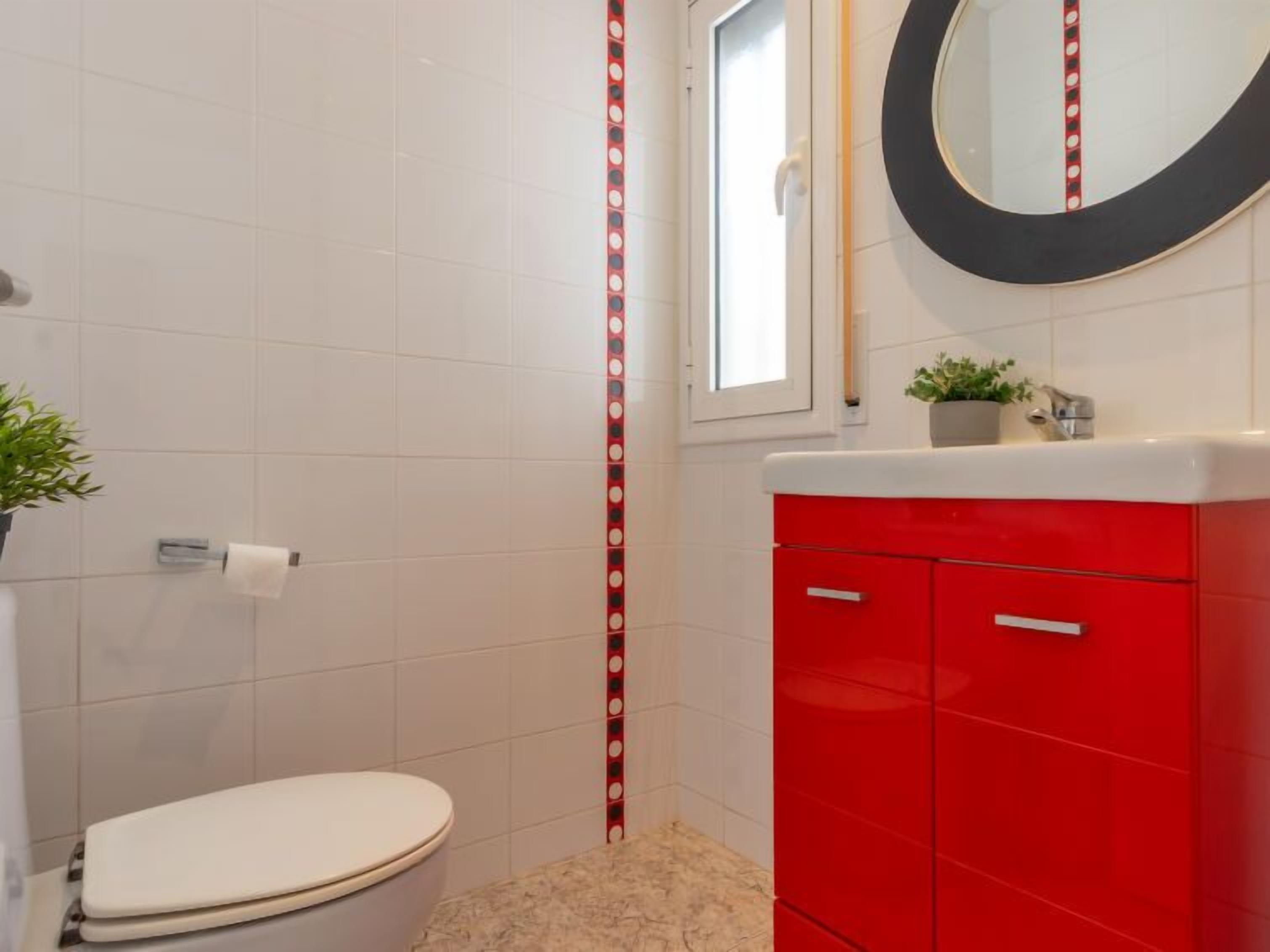 A bathroom with a white toilet, a red cabinet, a mirror, and a striped wall decoration.