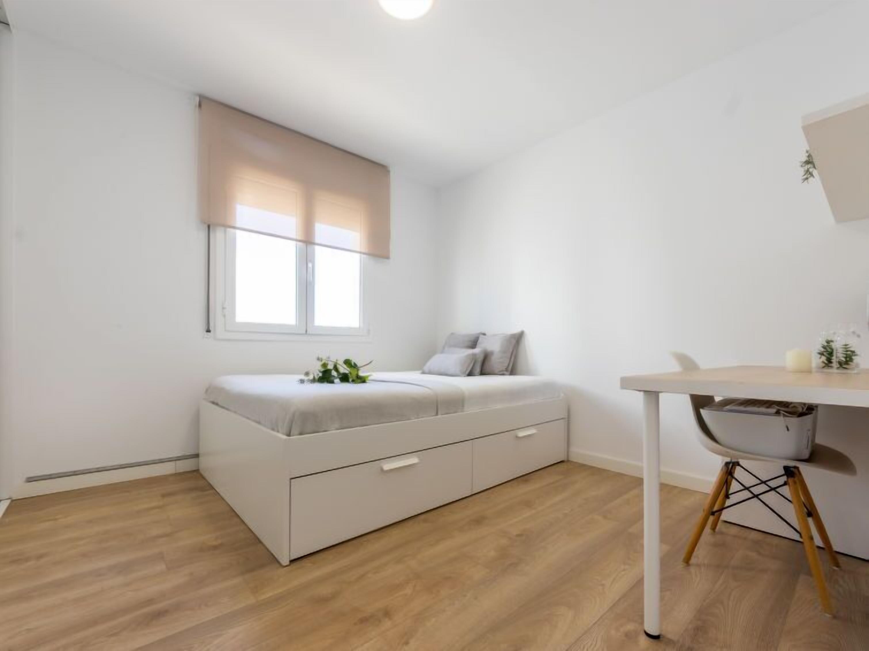 A minimalist bedroom with a bed, bedside table, and a desk with a chair.