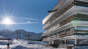Un bâtiment moderne à plusieurs étages, doté d’une façade en bois et de grandes fenêtres, situé dans une région montagneuse enneigée.