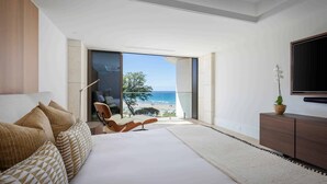 Un dormitorio moderno con una cama grande, vista a la playa y un televisor en la pared.