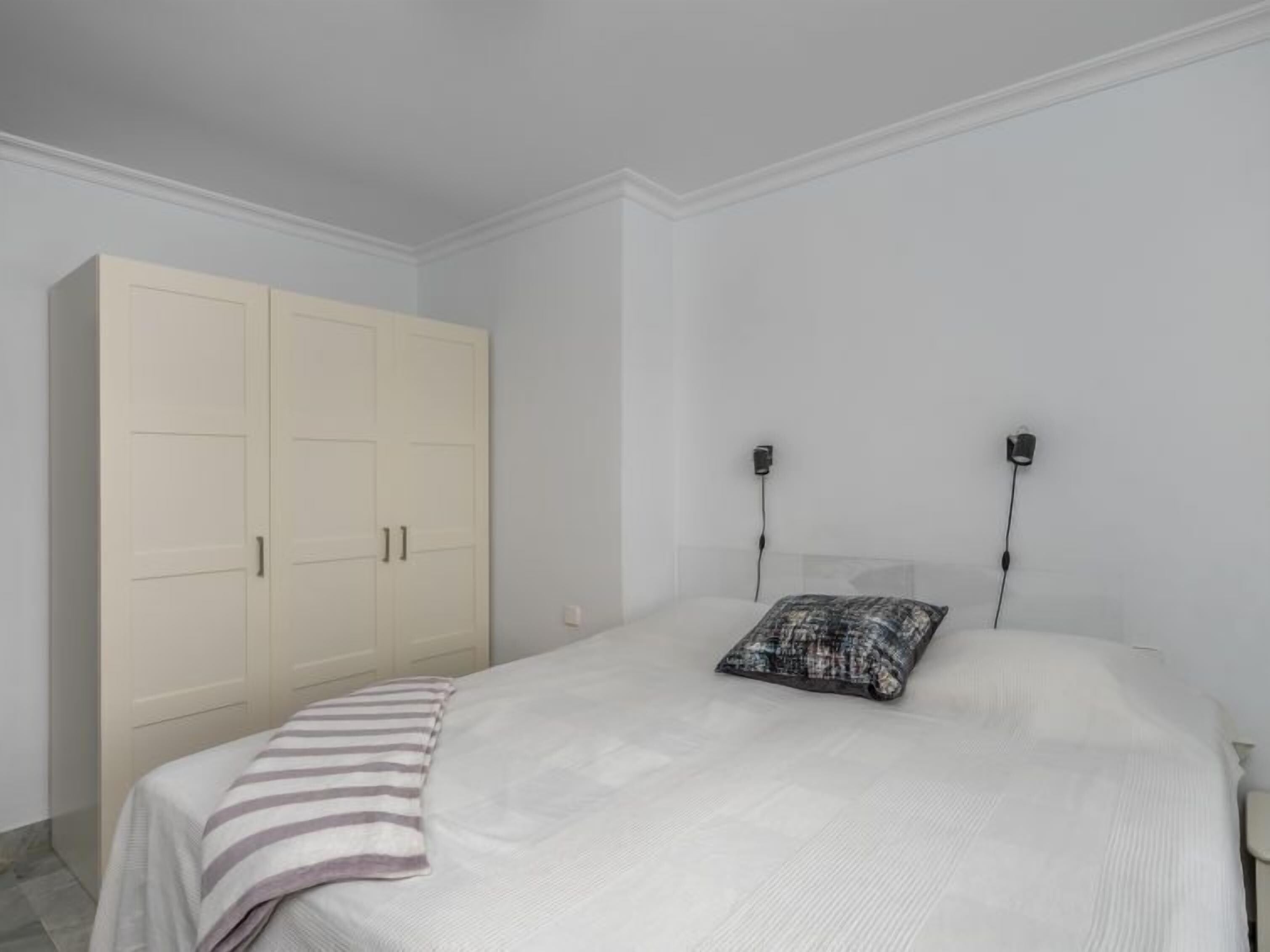 A bedroom with a bed, a large wardrobe, and two wall-mounted light fixtures.