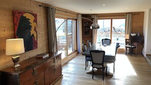 Une pièce spacieuse avec un plancher en bois, un coin repas comprenant une table et des chaises, une grande fenêtre avec des rideaux et un tableau accroché au mur.