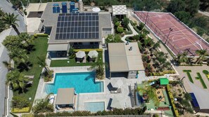Une propriété résidentielle dotée d’une piscine, de panneaux solaires, d’un court de tennis et d’un patio couvert.