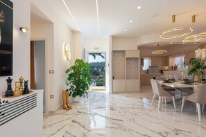 Une cuisine moderne avec un sol en marbre, un coin repas avec une table et des chaises, et une vue sur l’extérieur.