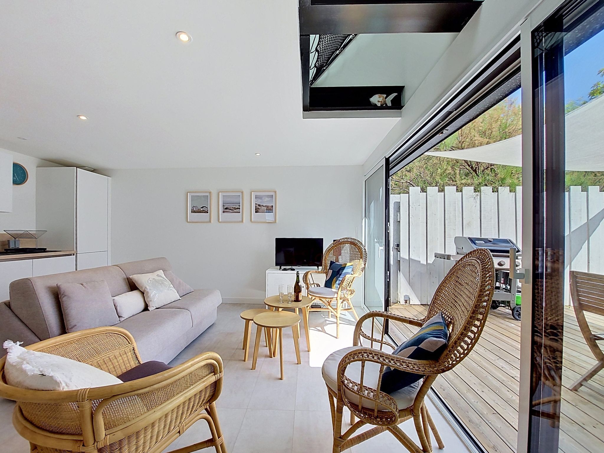 Een moderne woonkamer met een bank, rieten stoelen, een televisie en een barbecue buiten.
