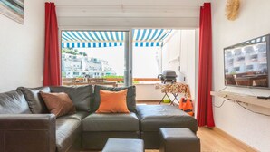 A living room with a black leather sofa, a television, and a grill outside the window.