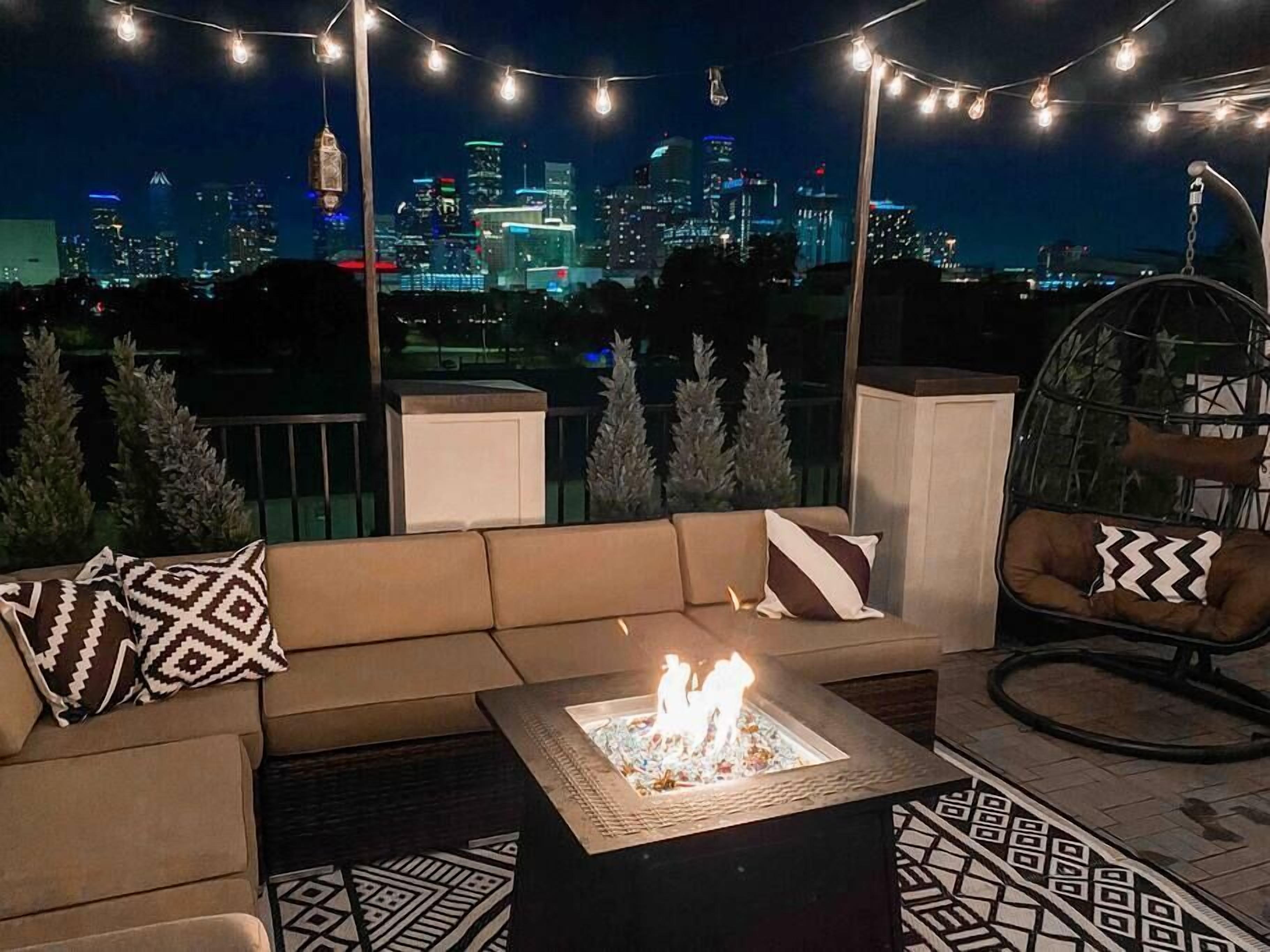 A rooftop terrace with a fire pit, seating area, and string lights.